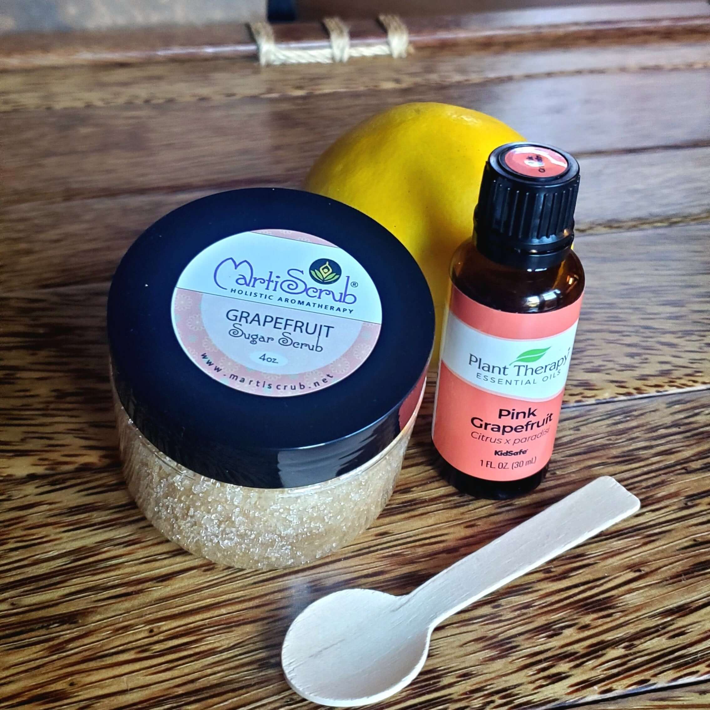 Grapefruit Sugar Scrub, essential oil, and fresh fruit on a wooden surface, perfect for exfoliating skin.