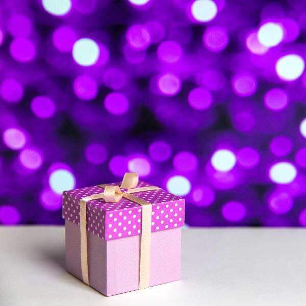 Gift-wrapped package with polka dot lid and bow, set against a purple bokeh background. Perfect for special occasions.