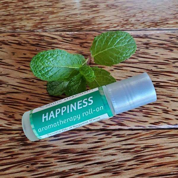 Happiness aromatherapy roll-on next to fresh mint leaves on a wooden surface.