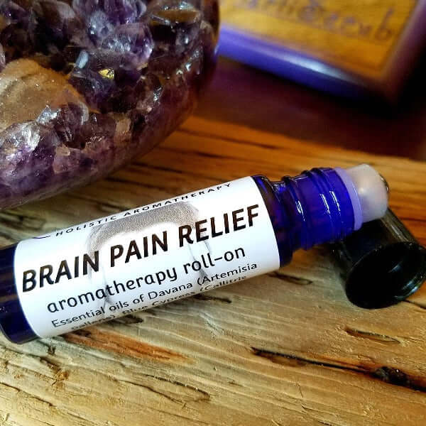 Brain Pain Relief essential oil roll-on bottle with Davana, set on a wooden surface with crystals in the background.