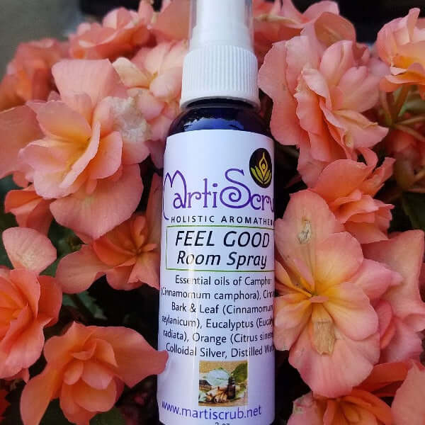 Feel Good Room Spray bottle amid pink flowers, highlights its citrus aroma and essential oil ingredients for freshening air.