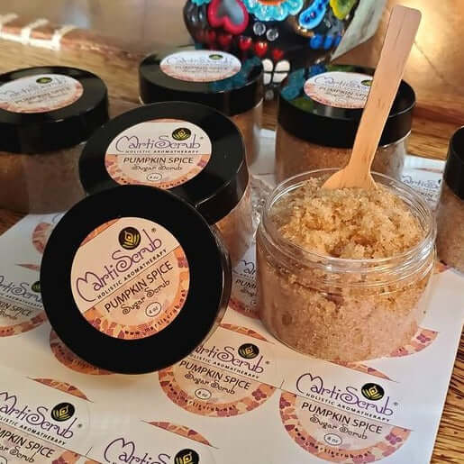 Pumpkin Spice Sugar Scrub jars with wooden spoons and labels on a wooden table, showcasing a natural skincare product.
