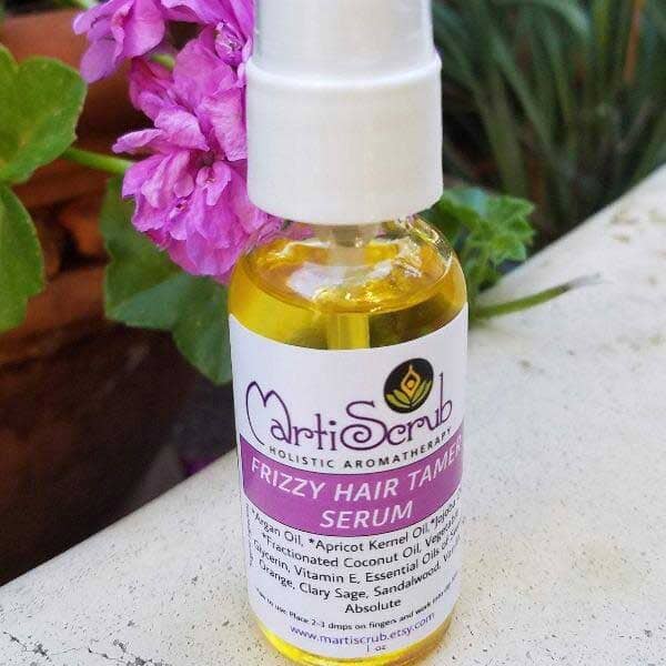 Frizzy Hair Tamer serum in a clear bottle surrounded by flowers, showcasing its nourishing ingredients for smooth hair.
