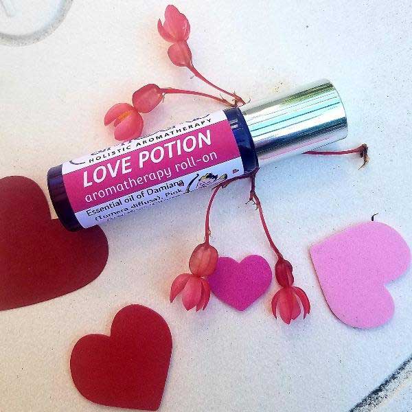 LOVE POTION Essential Oil Roll-On beside pink and red hearts, featuring Damiana and aromatherapy blend for romance.